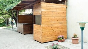 Eine Holzhütte mit geneigtem Dach, möglicherweise eine kleine Schutzhütte oder ein Kiosk, neben einer Mauer mit Blumentopf und Straßenlaterne.