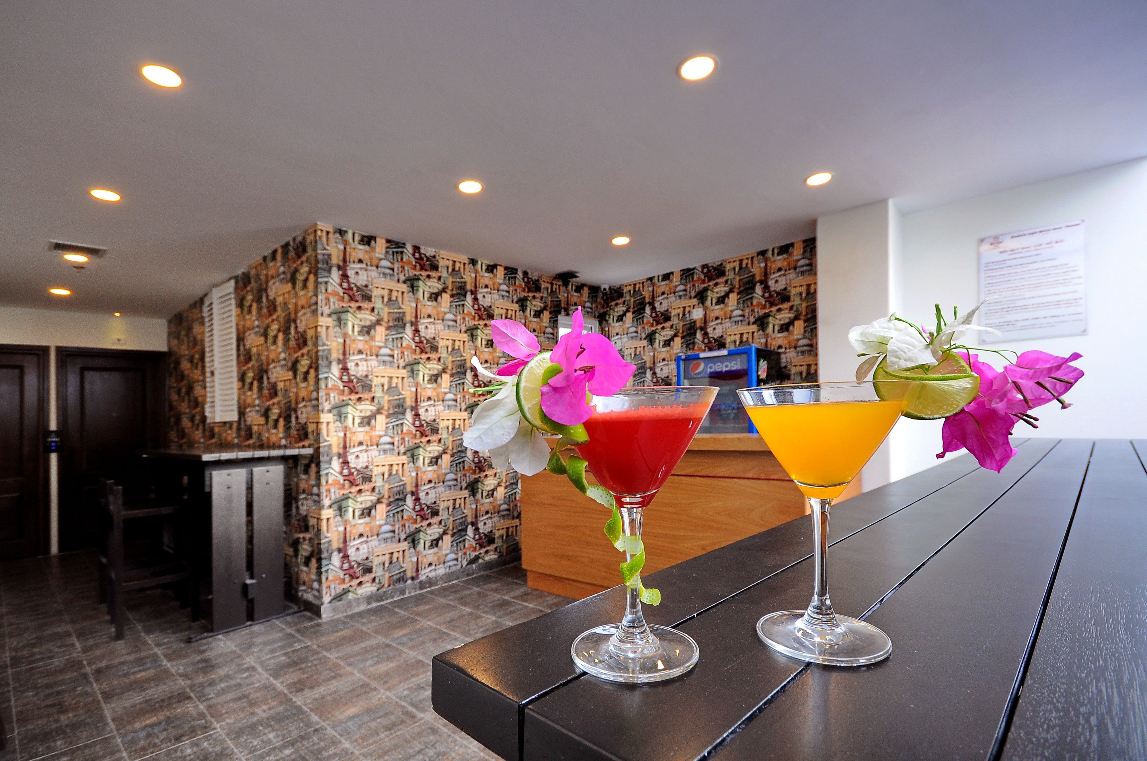 Eine Bar mit zwei Cocktails auf einem Tisch, einer Wand mit Muster und einem Empfangsbereich im Hintergrund.