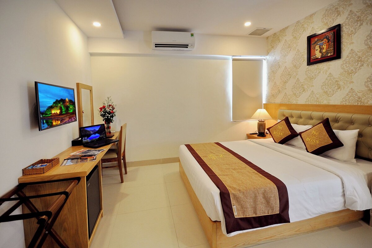A hotel room with a bed, desk, chair, laptop, and a television.
