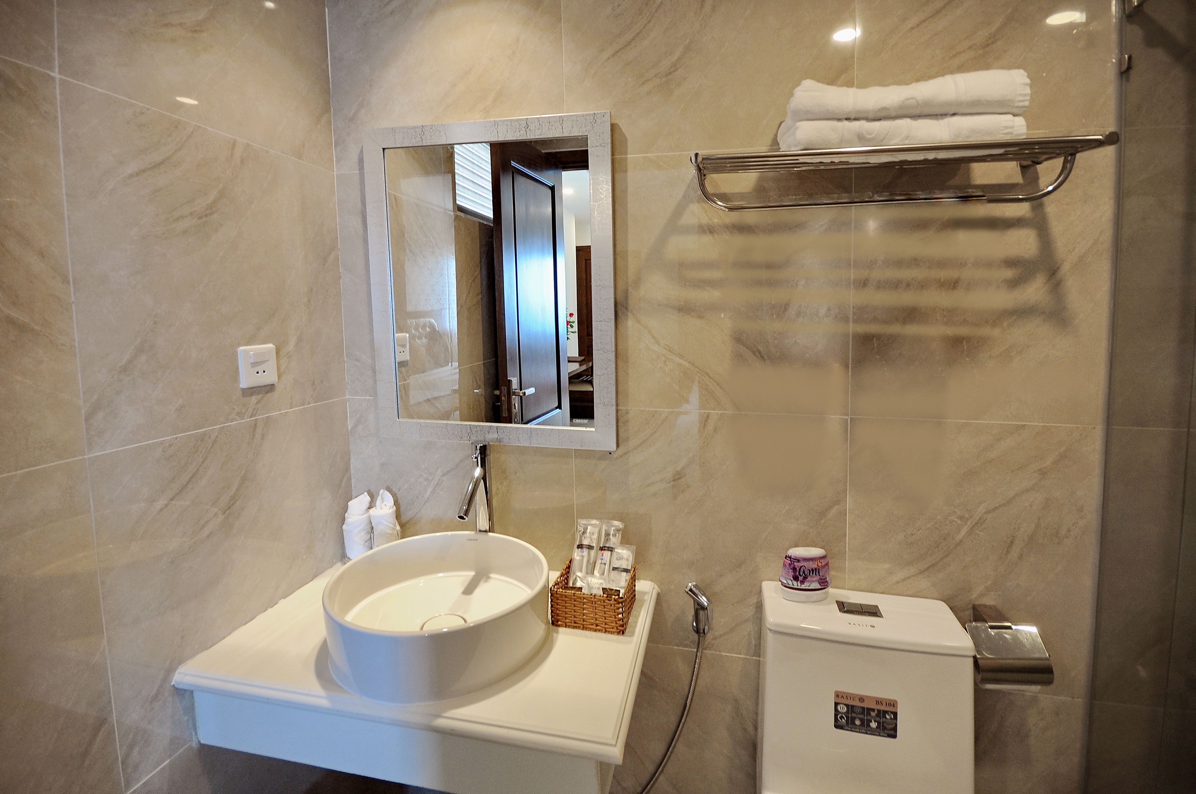 Un baño con lavamanos blanco, un espejo, toallero y un refrigerador pequeño.
