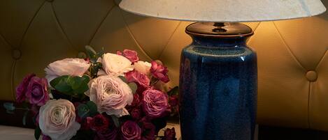 A bedside table with a blue lamp and a vase of flowers.