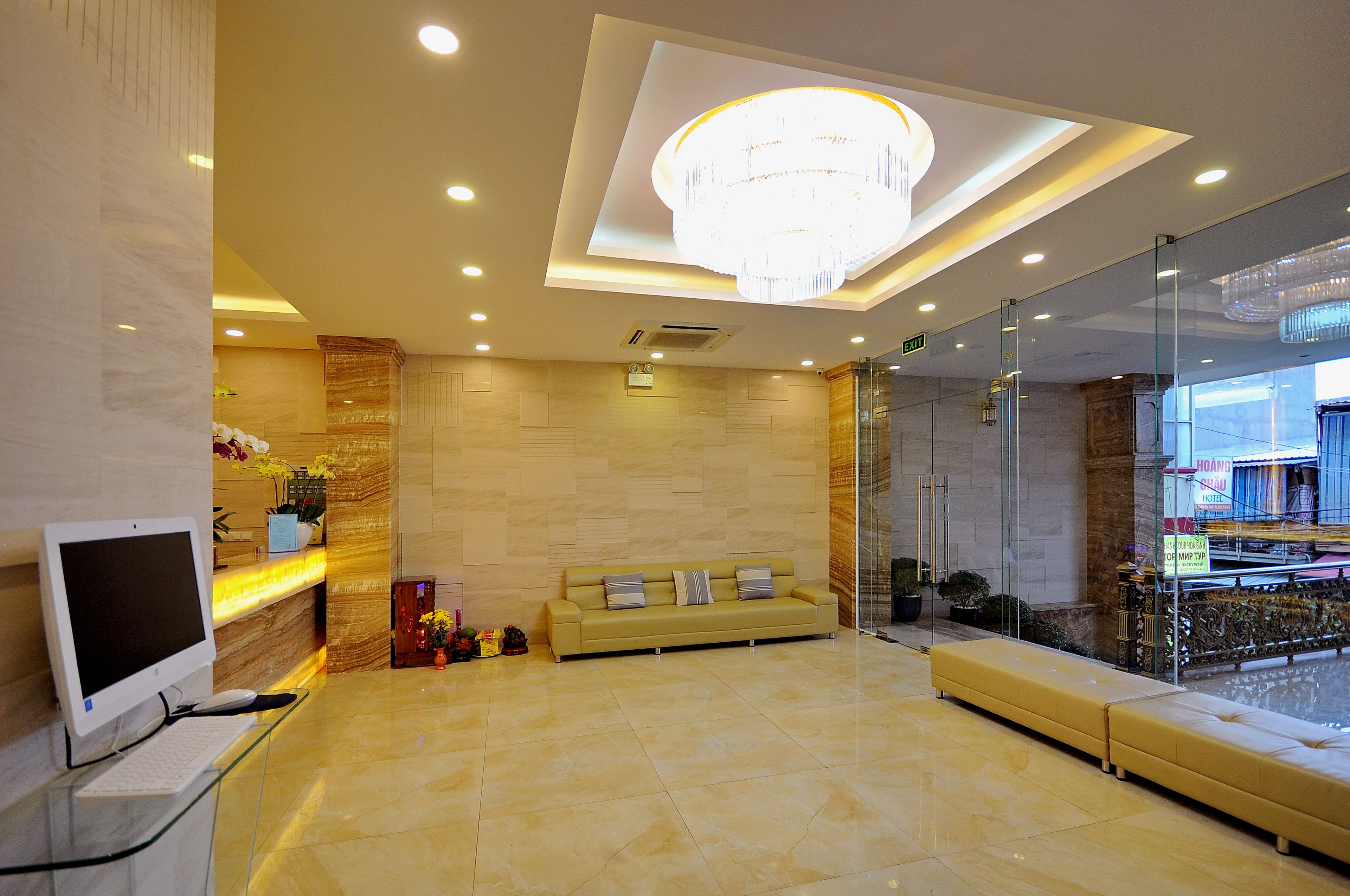 A modern hotel lobby with a reception desk, a sofa, and a large chandelier.