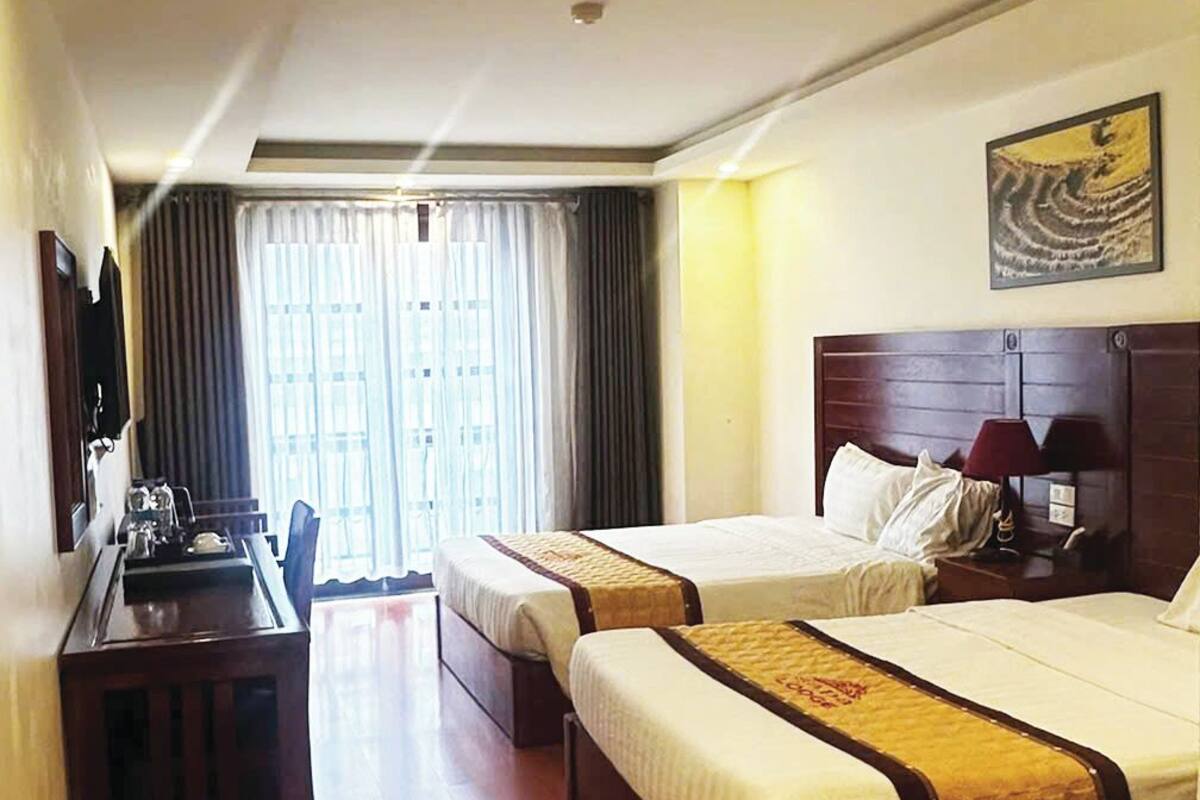 Ein Hotelzimmer mit zwei Betten, einem Schreibtisch, einem Stuhl, einem Fernseher und einem Fenster mit Vorhängen.
