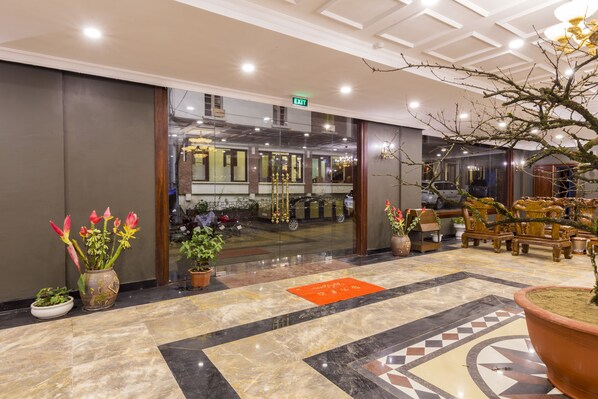 A hotel lobby with a marble floor, potted plants, and a reception area with a car parked outside.