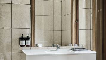 Un baño moderno con un espejo grande, un lavabo blanco y dos botellas de champú y acondicionador en la pared.