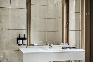 A modern bathroom with a large mirror, a white sink, and two bottles of shampoo and conditioner on the wall.