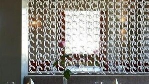 A restaurant interior with a chain-link partition, dining tables with chairs, and a vase with a single flower. - Rederiet Hotell (Farsund)