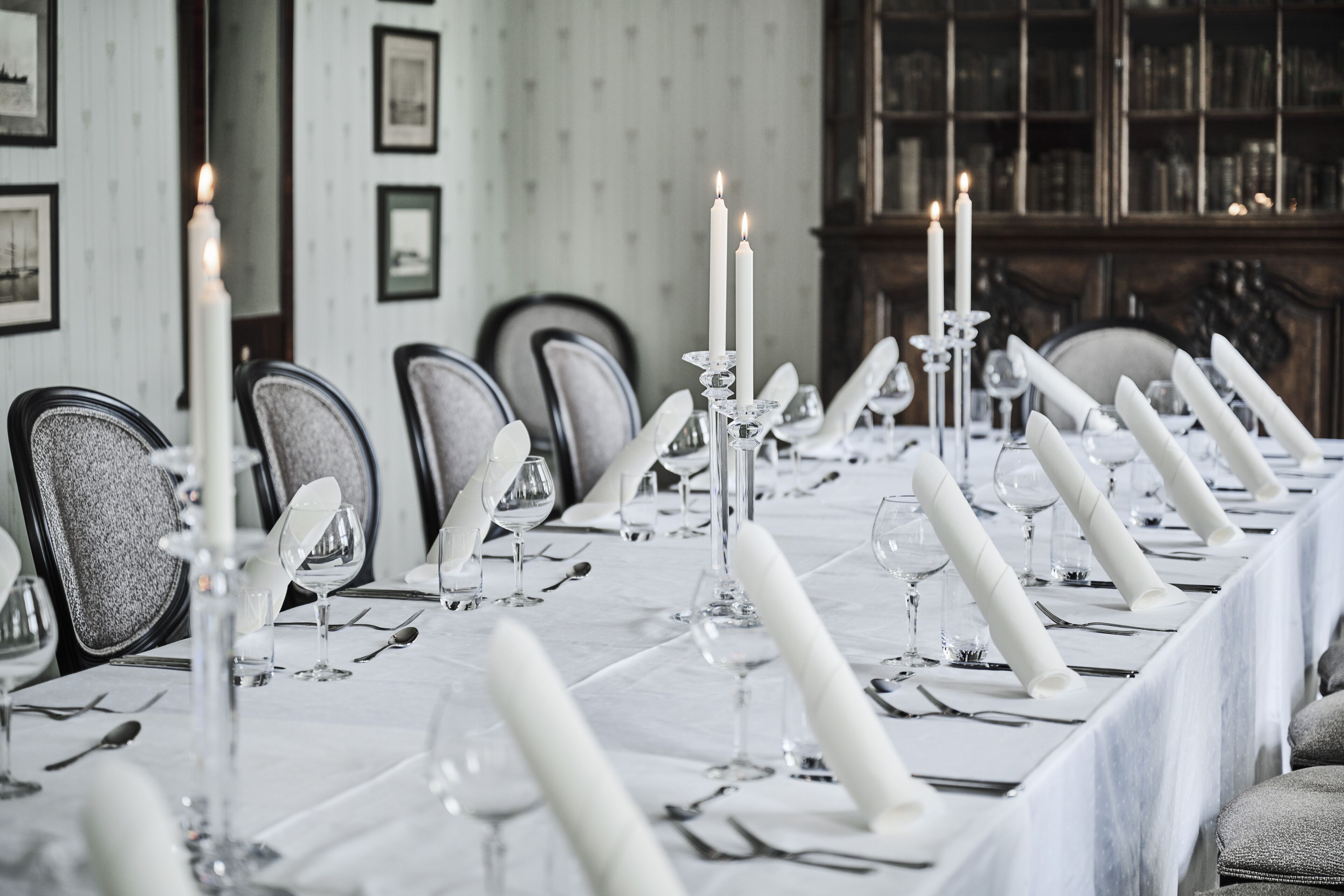 A formal dining room with a long table set for a meal, featuring white tablecloths, candles, and crystal candelabras.