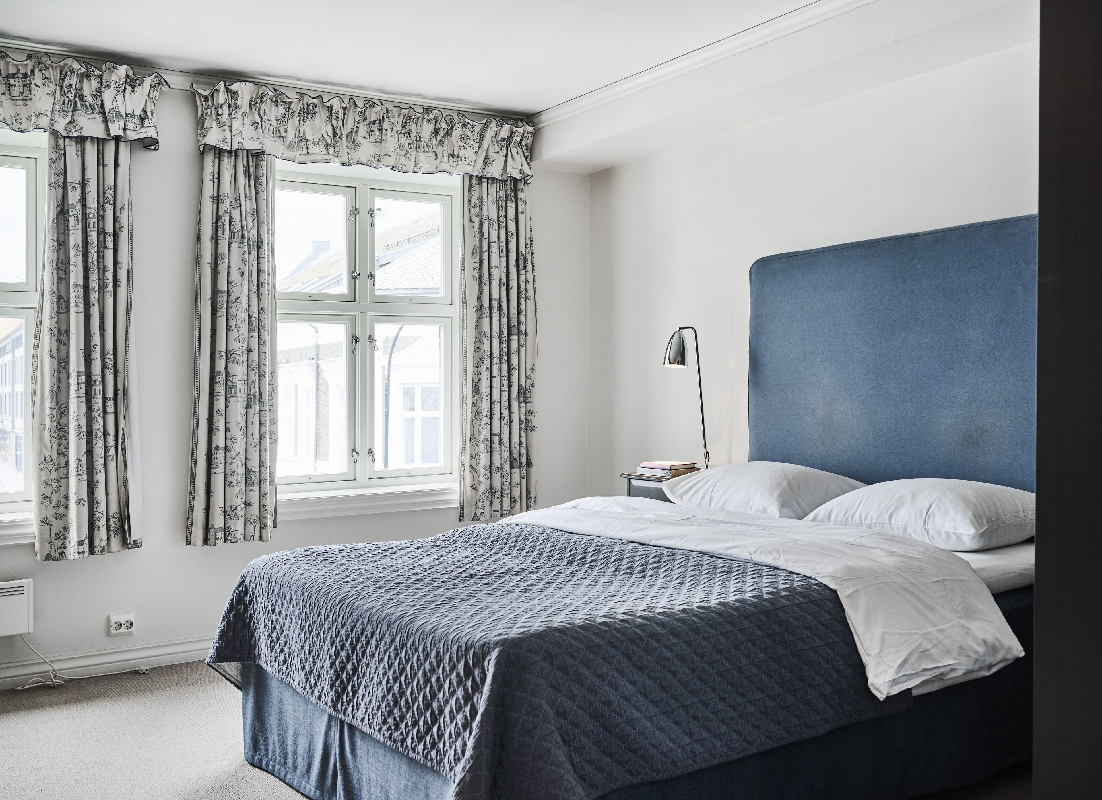A bedroom with a bed, a nightstand, a lamp, and a window with curtains.