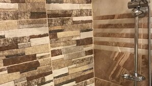 A shower area with a stone mosaic wall and a chrome showerhead. - Sun Rise Hotel (Amman)