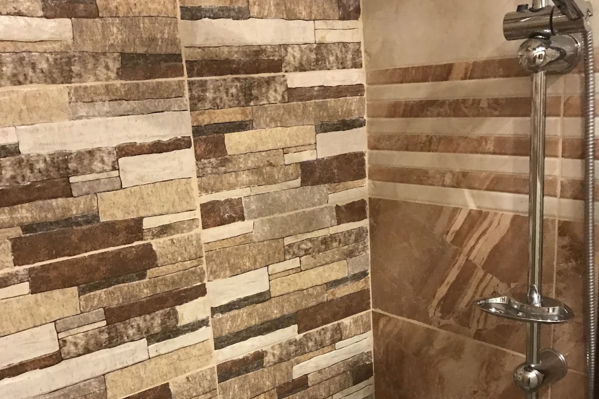 A shower area with a stone mosaic wall and a chrome showerhead.