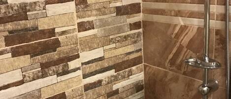 Un área de ducha con pared de mosaico de piedra y cabezal de ducha cromado.