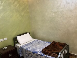A small, single-bed room with a green wall, a bedside table with a remote control, and a patterned bedspread. - Sun Rise Hotel (Amman)