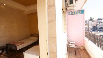 A hotel room with a single bed, a small table, and a balcony with a chair.