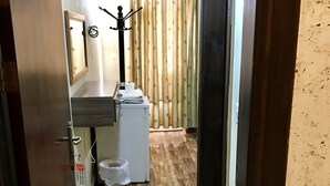 A narrow hallway with wooden flooring, a small kitchenette with a refrigerator, a sink, and a mirror. There is a door on the left and a curtain on the right. - Sun Rise Hotel (Amman)