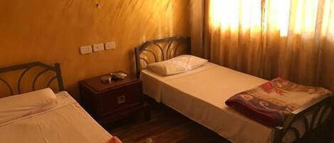 A room with two beds, wooden headboards, a nightstand, and a window with curtains.