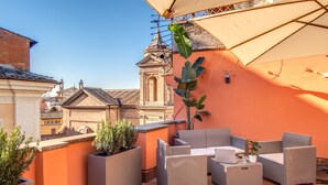 An outdoor seating area with wicker furniture, potted plants, and a large umbrella providing shade. - Piazza di Spagna Comfort Rooms (Rome)