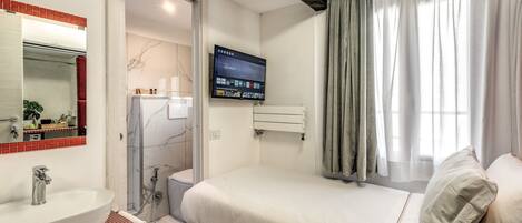 A modern bedroom with a large bed, a built-in TV, a bathroom with a shower, and a red-tiled sink area.