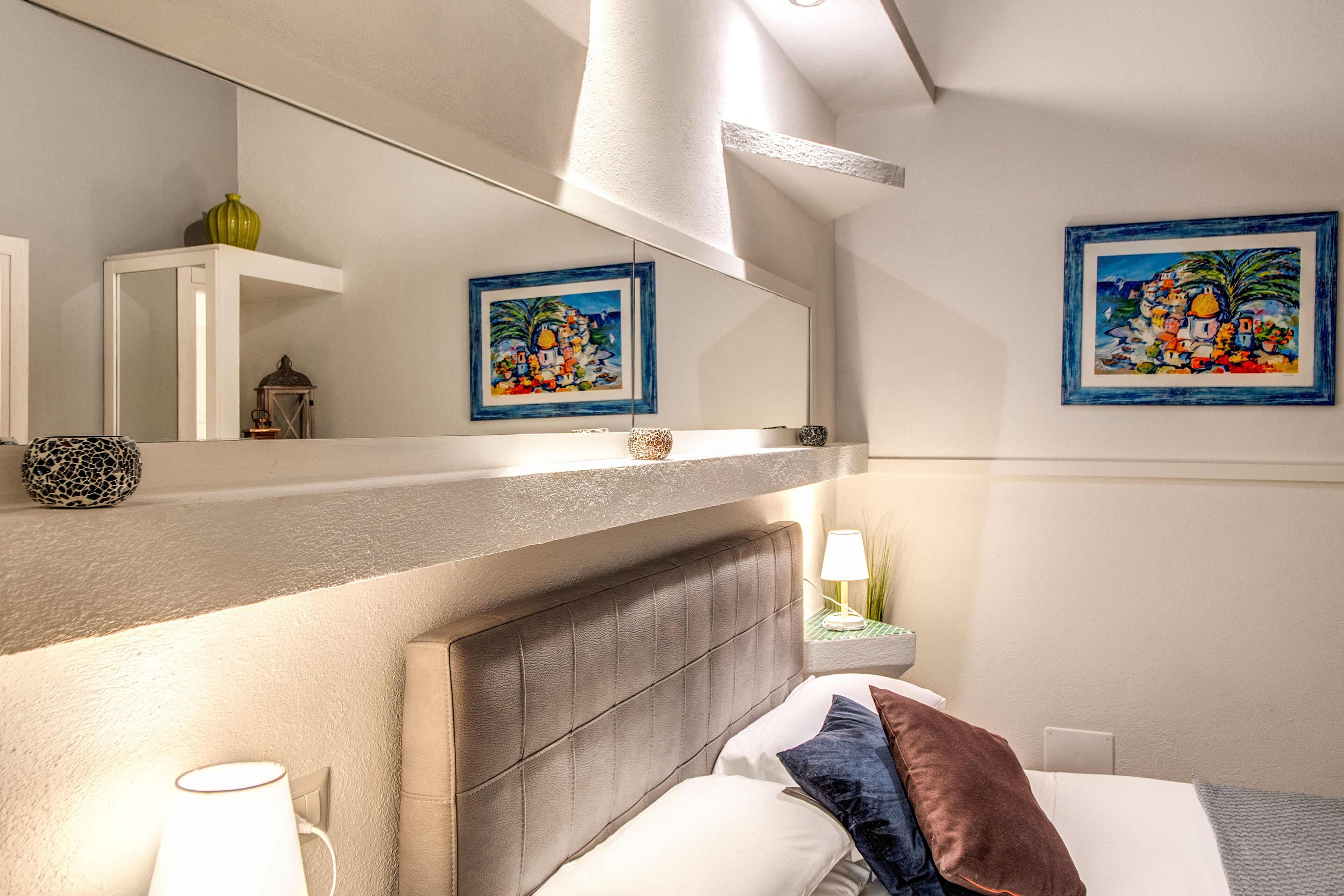 Une chambre d’hôtel avec un lit, des lampes de chevet, un miroir et deux tableaux encadrés accrochés au mur.