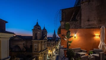 A rooftop terrace with a view of historic buildings, outdoor seating, and a decorative wall.