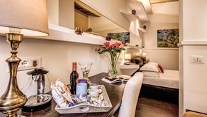 A hotel room with a dining table set with various items, a bed with pillows, a vase with flowers, and a painting on the wall. - Piazza di Spagna Comfort Rooms (Rome)