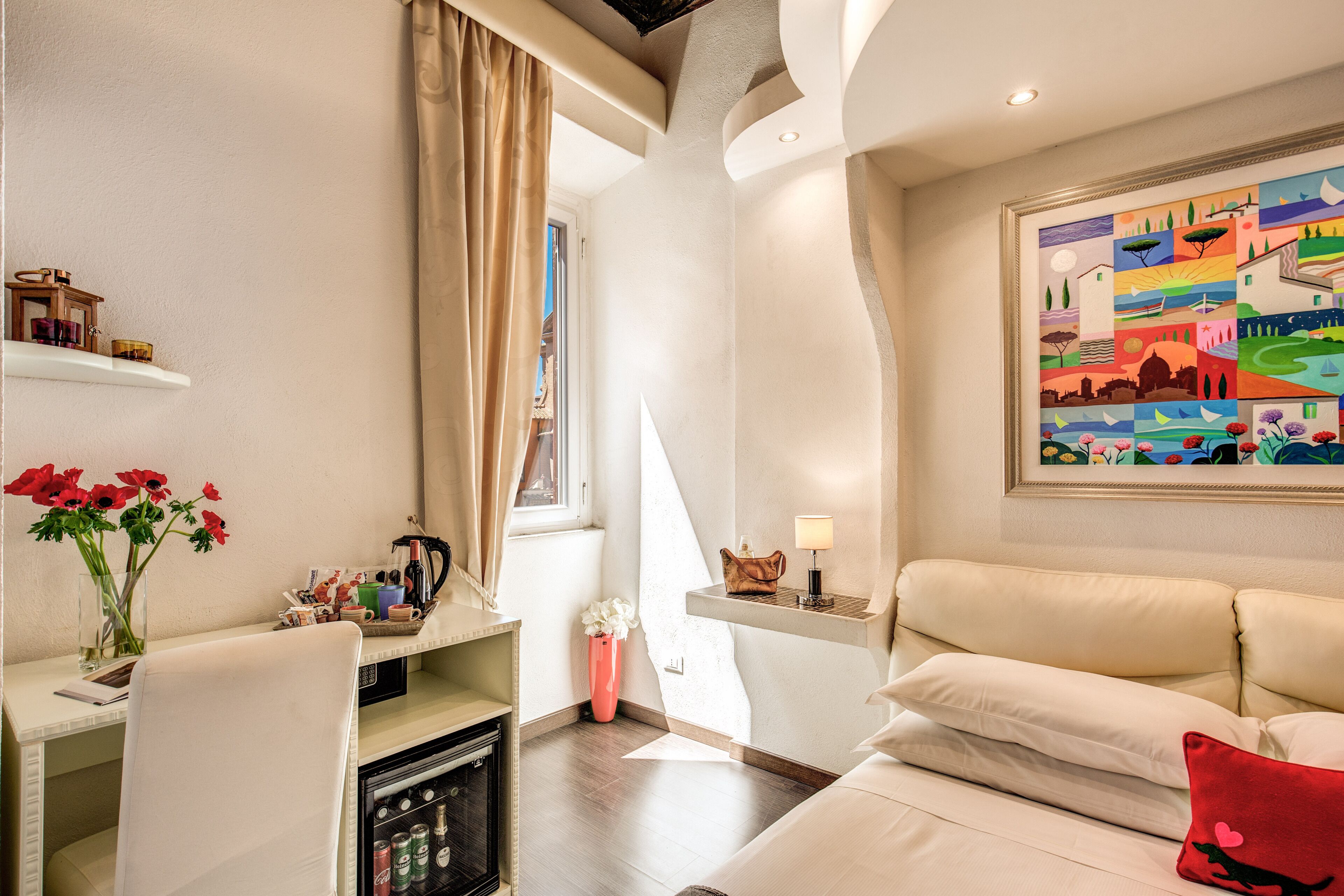 Une chambre d’hôtel moderne avec un canapé blanc, un bureau avec un ordinateur, une machine à café et un tableau au mur.