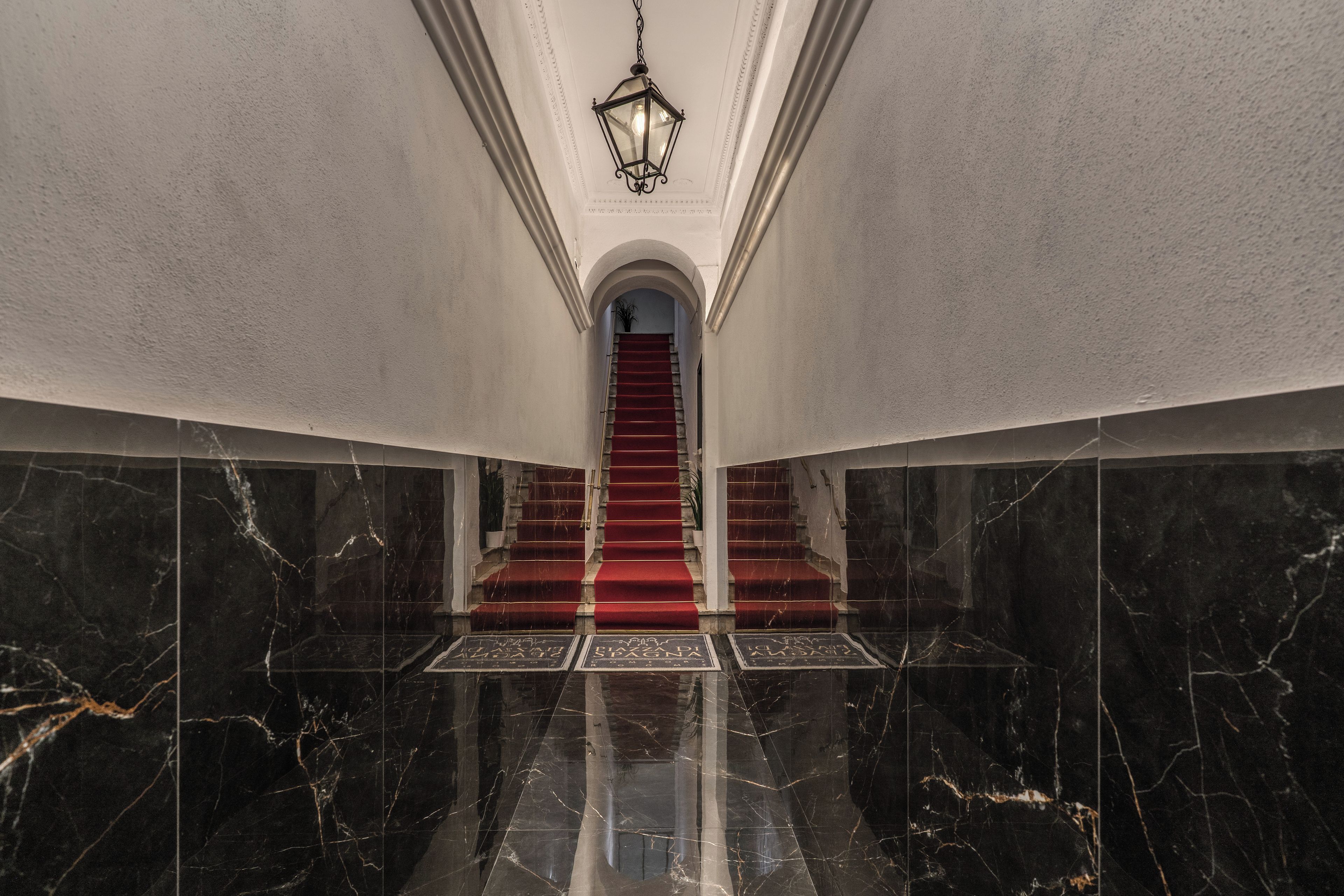 Un magnifique escalier, avec des marches recouvertes de moquette rouge, menant à une porte en arc de cercle.