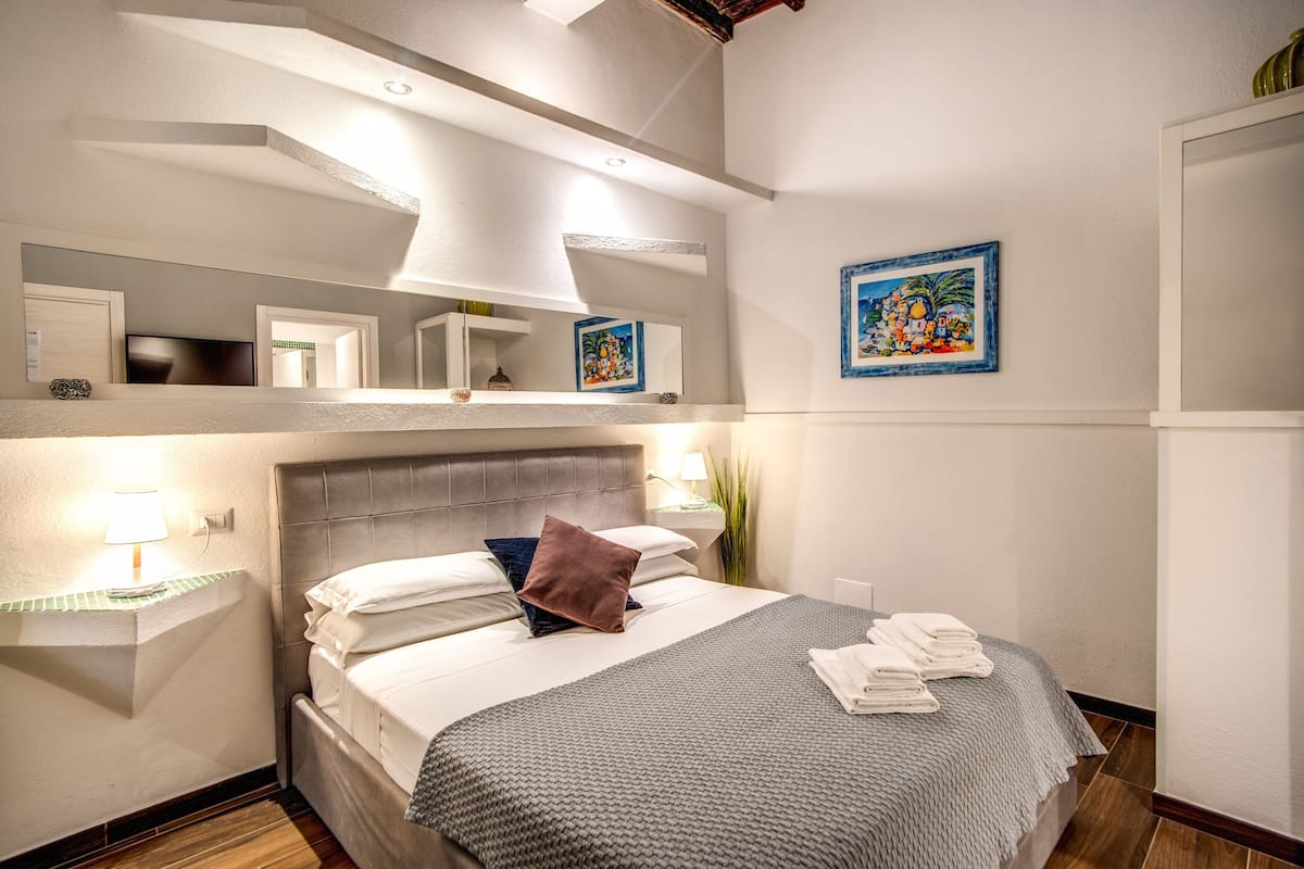 A hotel room with a large bed, a nightstand, a mirror, and artwork on the walls.