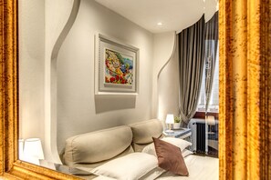 Een hotelkamer met een bed, nachtkastje, lamp, een kunstwerk in een lijst aan de muur, en een raam met gordijnen.