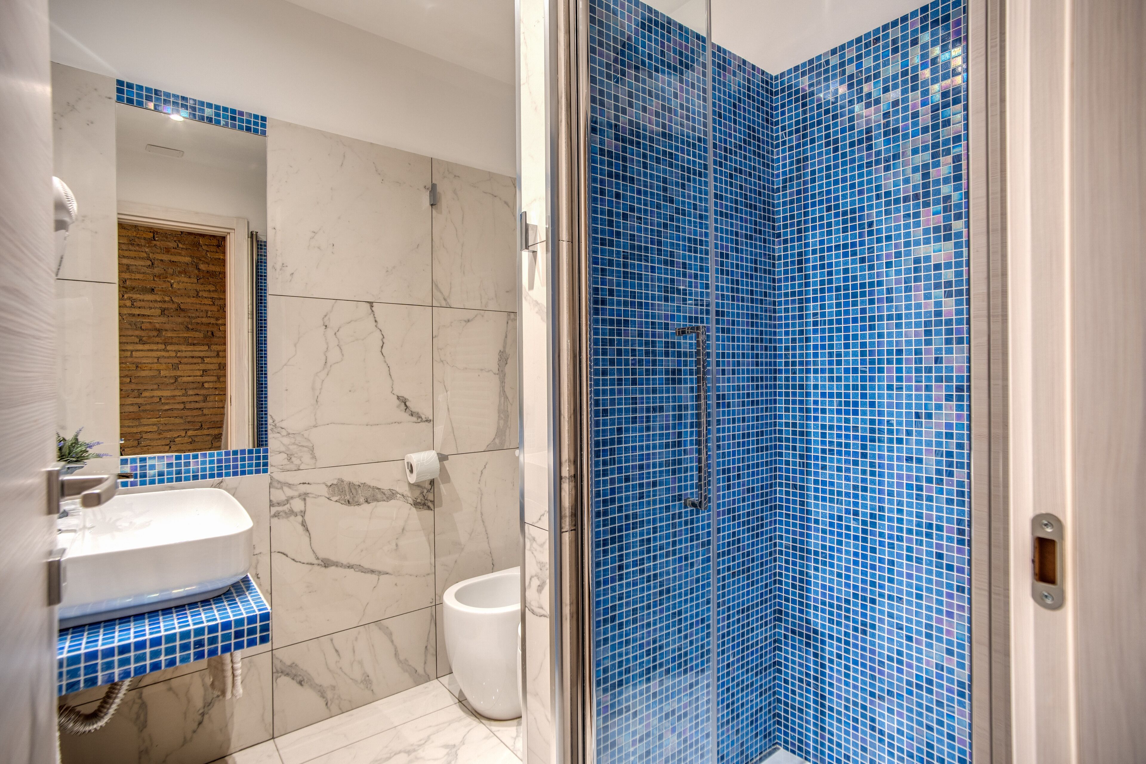 Un baño con lavamanos blanco, inodoro y ducha con mosaicos azules.