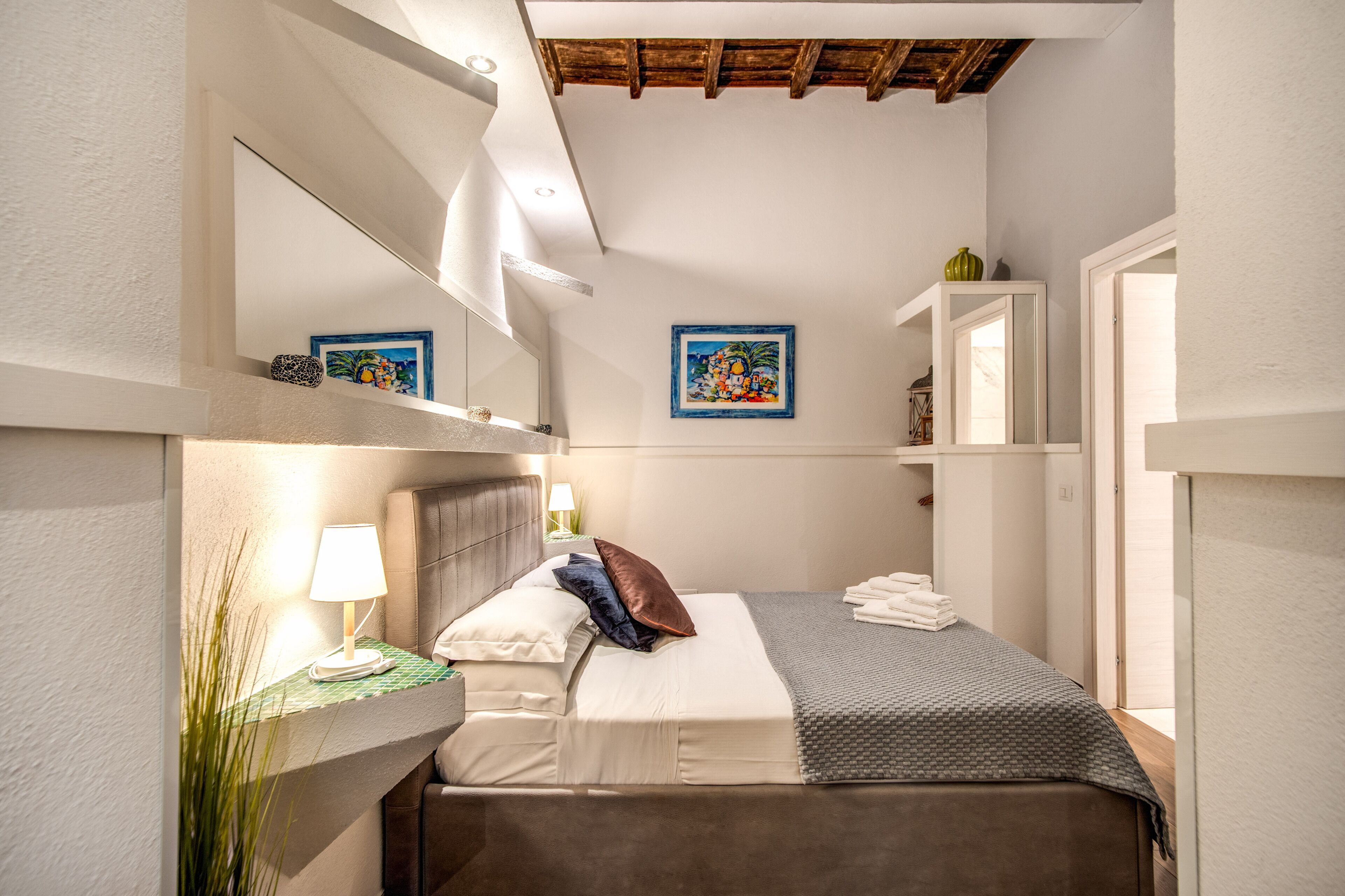 A bedroom with a bed, bedside lamp, and a painting on the wall.