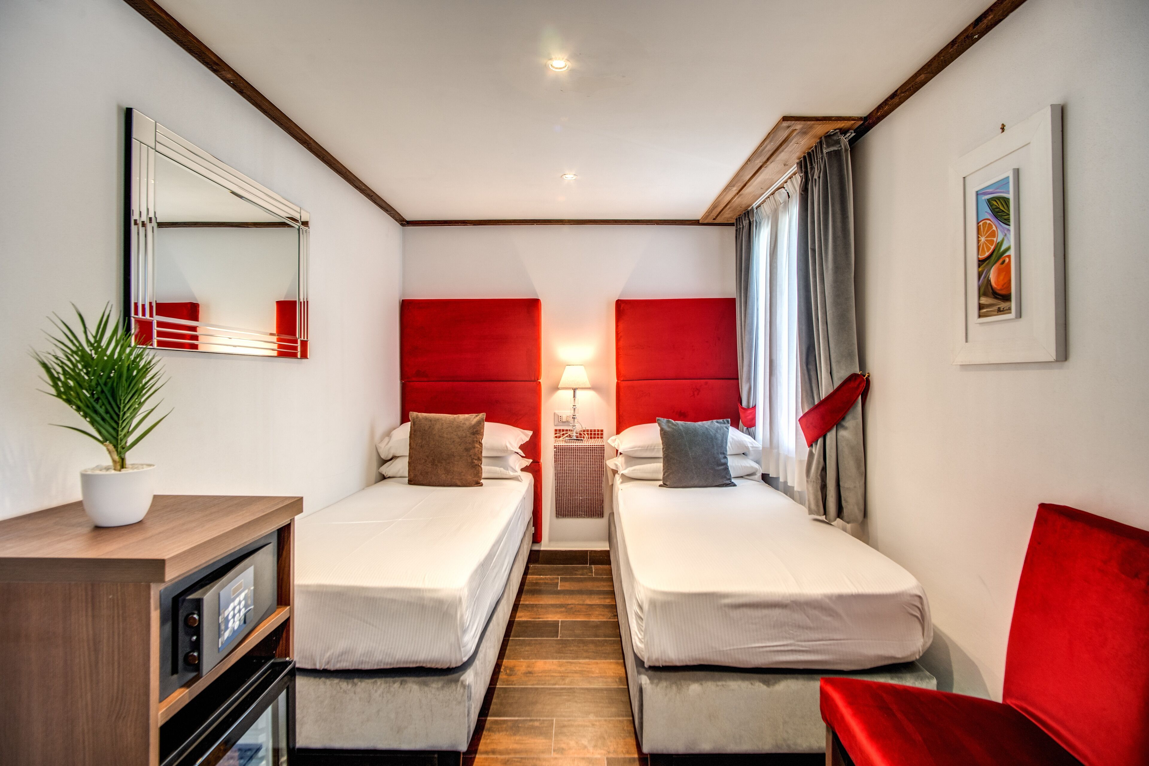 Een hotelkamer met twee bedden, een bureau, een spiegel, een lamp en een rode stoel.