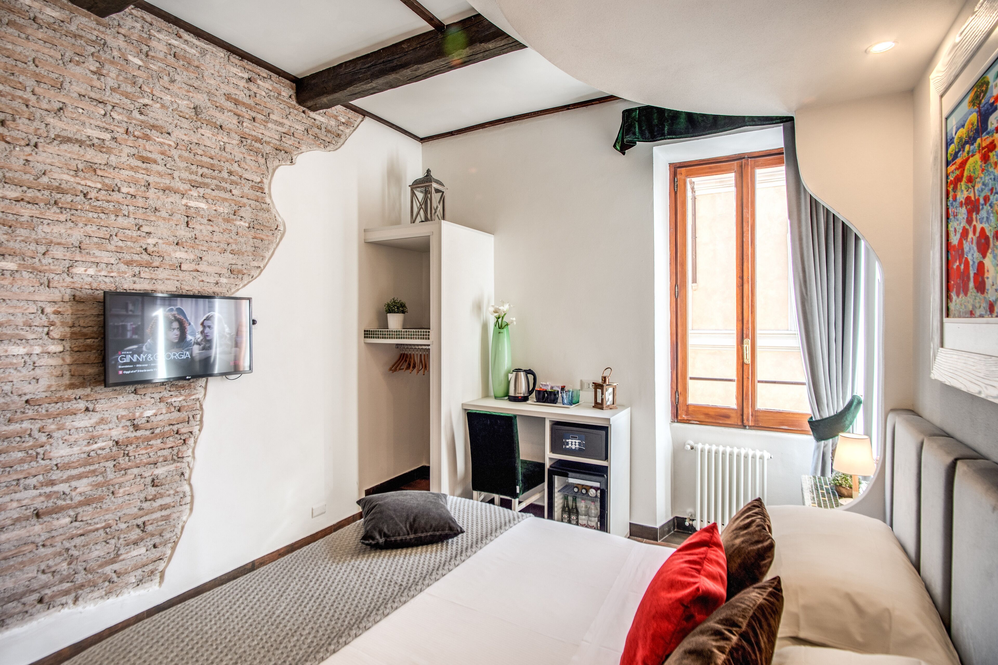 Une chambre d’hôtel avec un mur en briques, un lit avec des oreillers, une télévision, un bureau avec une bouilloire et une fenêtre avec des rideaux.