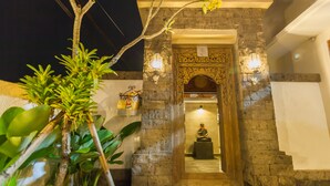 A stone entrance with a statue, decorative lighting, and lush greenery. - Jani's Place Cottage (Ubud)