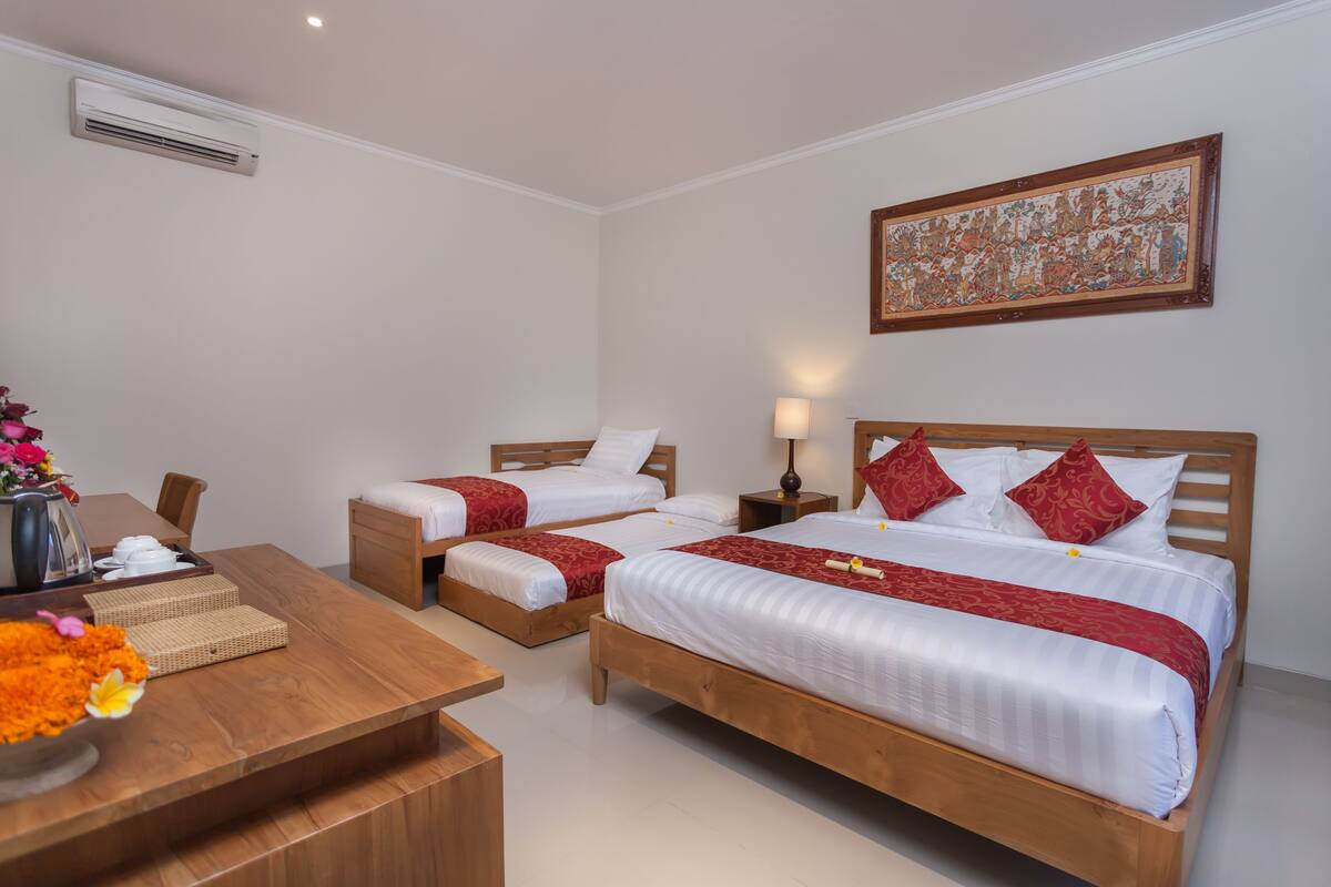 A hotel room with two single beds, a wooden desk, a vase with flowers, and a framed artwork on the wall.