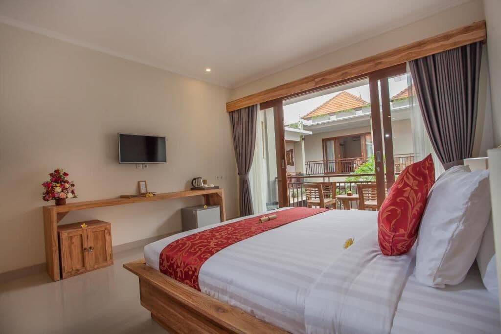A hotel room with a large bed, a TV mounted on the wall, a wooden cabinet, and a balcony with outdoor furniture.