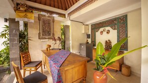 A wooden dining table with a patterned tablecloth, two wooden chairs, and a potted plant. - Jani's Place Cottage (Ubud)