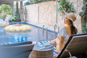 A pool area with lounge chairs and a statue in the background. - Jani's Place Cottage (Ubud)