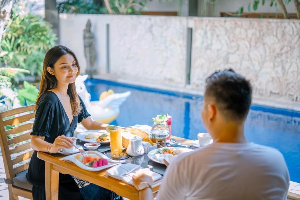 A dining table with plates of food and drinks, a pool in the background, and a stone wall.