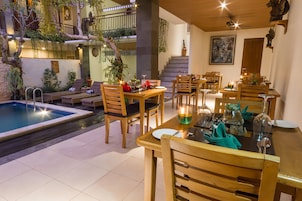 Un comedor con mesas y sillas de madera, una piscina y plantas de interior.