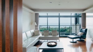 A spacious living room with a large window offering a view of the sea. There is a white sofa, a black armchair, and a coffee table. - Adagio Shitiping (Fengbin)