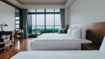 Habitación de hotel con una cama grande, un escritorio con silla y vistas a zonas verdes a través de amplios ventanales.