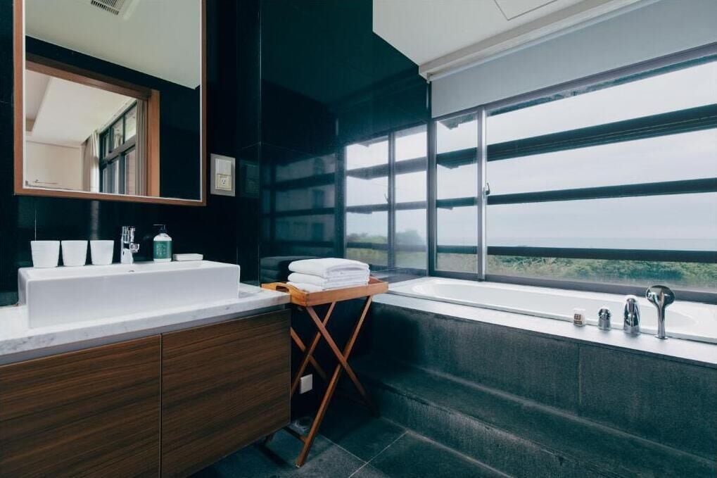 Un baño moderno con un espejo grande, dos lavamanos, una bañera y un ventanal con vistas.