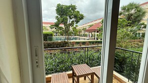 Un balcón con dos mesas de madera, una piscina y vistas a un edificio con tejado rojo.