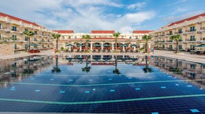 A large swimming pool with clear blue water, surrounded by a hotel with multiple balconies and outdoor seating areas. - Sokha Palace Siem Reap Hotel (Siem Reap)