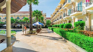 Un patio de hotel con piscina, palmeras y una zona de estar cubierta.