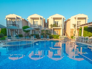 A swimming pool with lounge chairs and umbrellas, surrounded by multi-story buildings with balconies. - Kalina Otel (Datça)