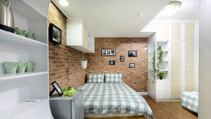 Een slaapkamer met een bakstenen muur, een bed met geruit beddengoed, planken met groene vazen en een hangplant.