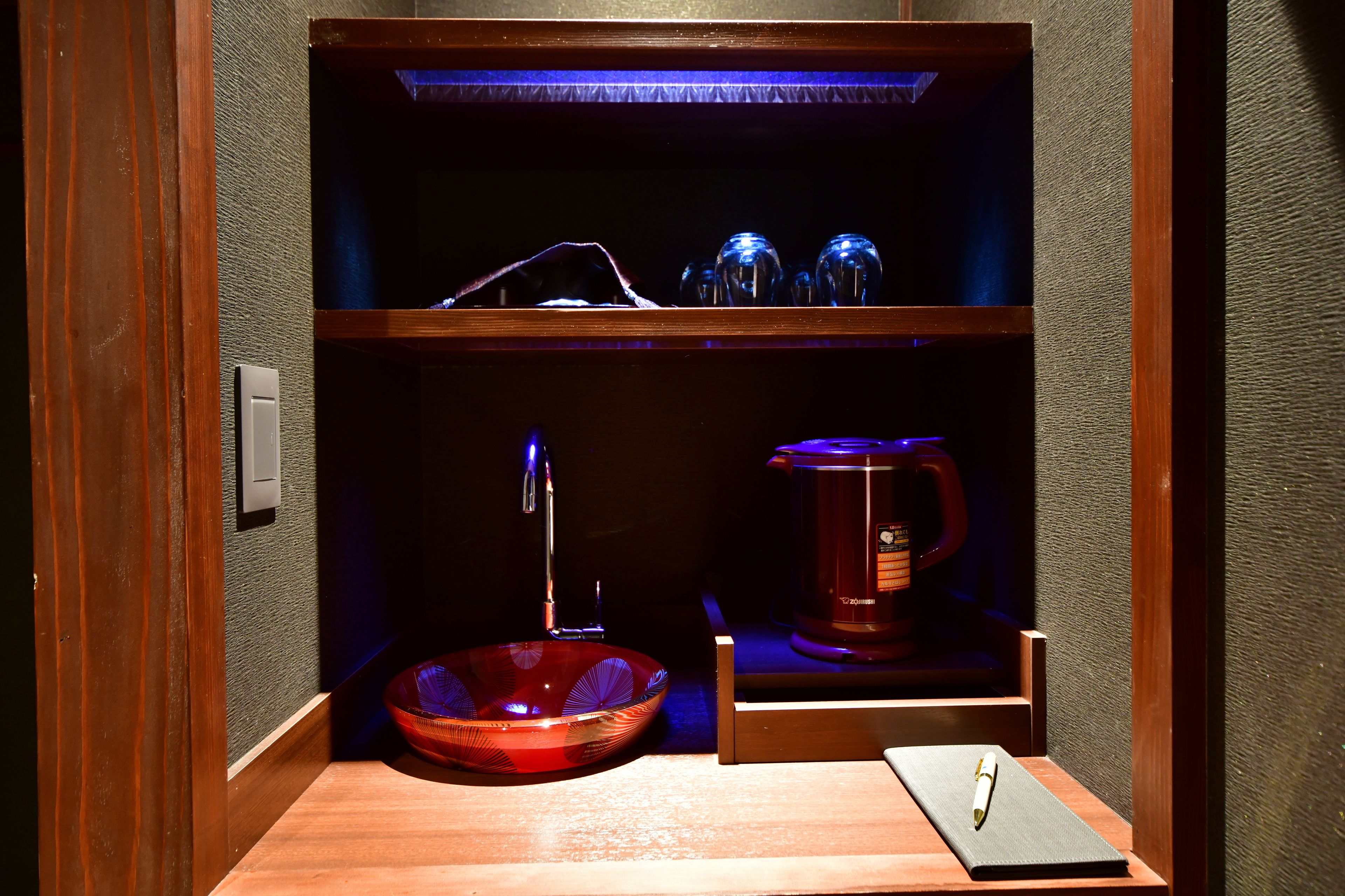 Une petite salle de bain avec un meuble-lavabo en bois, un lavabo en verre, une machine à café et une petite étagère avec de la verrerie.