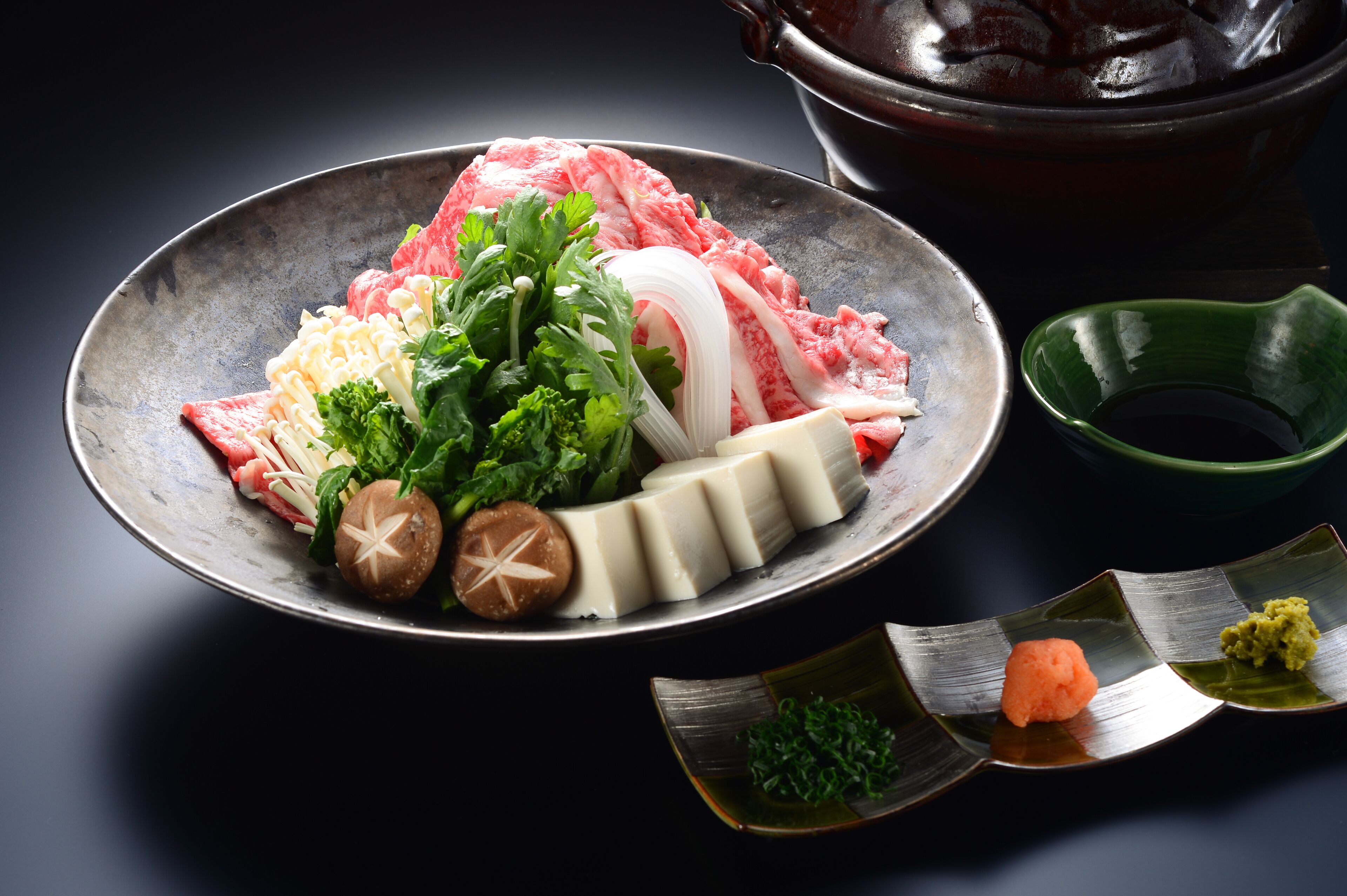 A plate of raw fish, vegetables, and tofu on a dark table.